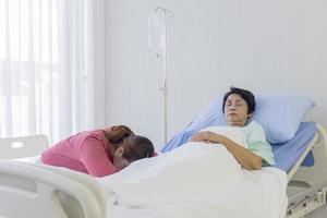 en äldre asiatisk kvinna är sjuk och sover i sängen bredvid sin dotter och sov i sin sjukhussäng. foto