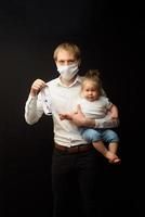 pappa i en medicinsk mask håller sin lilla dotter. konceptet att skydda barn under epidemin av coronavirus foto