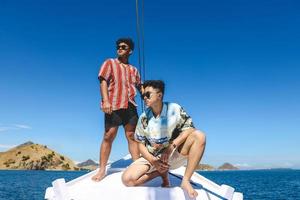 två asiatiska man som bär solglasögon poserar på en båt medan du tittar mot havet foto