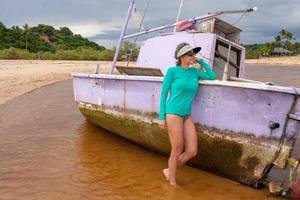 dam poserar bredvid en gammal övergiven och halvt sjunken gammal fiskebåt vid praia dos nativos, i trancoso, bahia, brasilien foto