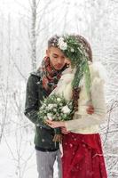 vackra brud och brudgum med en vit hund står på bakgrunden av en snöig skog. foto