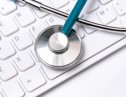 stetoskop på datorns tangentbord på vit bakgrund. läkare skriver medicinskt fall långtidsvård behandlingskoncept, närbild, makro, kopia utrymme foto
