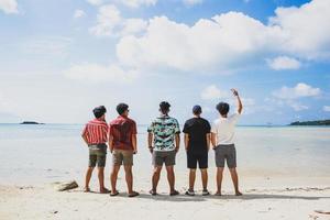 bakifrån av en grupp vänner som njuter av sommarsemestern på den tropiska stranden foto