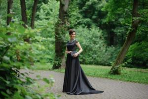 ung vacker kvinna poserar i en svart klänning i en park. foto