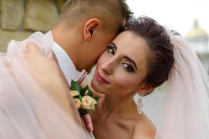 brudparet kramas under en slöja och böjde försiktigt sina huvuden mot varandra. foto