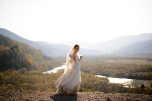 porträtt av en ung vacker brud i bergen med en slöja. vinden utvecklar en slöja. bröllopsfotografering i bergen. foto