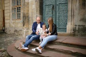 föräldrar och deras dotter sitter på trappan till en gammal kyrka. foto