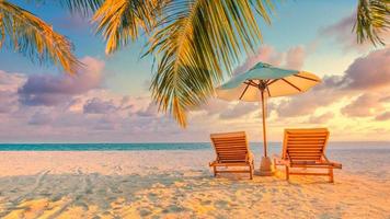 vackert tropiskt solnedgångslandskap, två solstolar, solstolar, paraply under palmen. vit sand, havsutsikt med horisont, färgglad skymningshimmel, lugn och avkoppling. inspirerande strandhotell foto