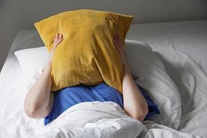 trött håglös person som ligger i sängen och gömmer ansiktet under kudden foto