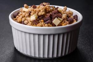 välsmakande hälsosam frukost med flingor, granola, choklad, mjölk och sylt på en mörk betongbakgrund foto