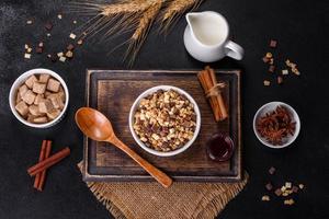 välsmakande hälsosam frukost med flingor, granola, choklad, mjölk och sylt på en mörk betongbakgrund foto