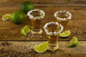 tre tequilashots med lime och salt på träbakgrunden foto