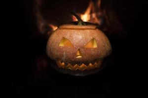 läskig halloween pumpa nära en öppen spis. eld i bakgrunden. foto