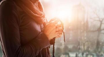kristen religion och hopp koncept. kvinna händer ber med radband och träkors. välsigna gud som hjälper katolik på kyrklig bakgrund. foto