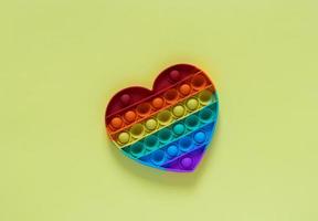 color pop it antistress leksak för barn. regnbåge hjärta formad isolerad på gul bakgrund. pop it leksak. foto