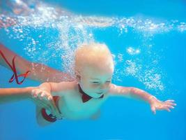 liten pojke spädbarn med röd fjäril dykning under vattnet i poolen, lära sig simma. sport och semester koncept foto
