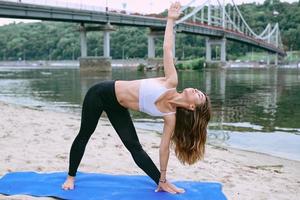 ung vältränad kvinna i sportkläder i olika yoga-asanas utomhus på stranden vid floden. yoga och sport koncept foto