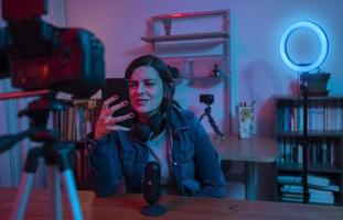 vacker latinamerikansk kvinna framför en videokamera som spelar in en blogg i sin studio med rött och blått ljus inne i hennes hus foto