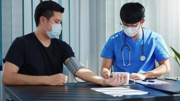 asiatisk läkare använder en patients blodtrycksmätare vid tidpunkten för sin årliga kontroll och förklarar hans blodtryck. foto