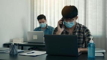 asiater sitter på sitt kontor och använder telefonen för att prata med kunder medan de bär masker på sina kontor under covid-19. foto