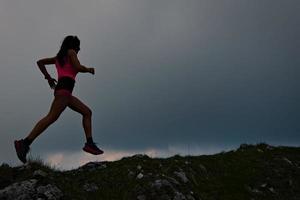 sportig tjej med vacker atletisk kropp springer i den alpina åsen i skymningen foto