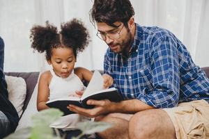 litet sött barn som ser förvånat ut älskar att läsa bok och lära sig stöd från pappa till smart barnkoncept. foto