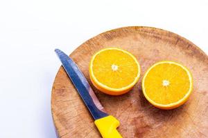 apelsinen är halva bollen och knivar placerade på skärbrädan på den vita bakgrunden foto