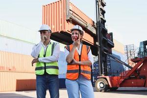 porträtt av två arbetare bär skyddsväst och hjälm diskuterar på logistisk frakt last container varv, senior ingenjör man pratar med vacker ung kvinna kollega på arbetsplatsen. foto