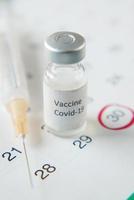 coronavirusvaccin, spruta och kalender på bordet foto