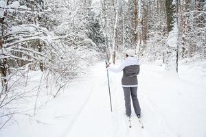 skidåkare en kvinna i en membranjacka med skidstavar i händerna med ryggen mot bakgrunden av en snöig skog. längdskidåkning i vinterskogen, utomhussporter, hälsosam livsstil. foto