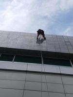 foto av en arbetare som städar utsidan av byggnaden, hängande i ett säkerhetsrep