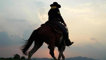 siluett cowboy på hästryggen mot en vacker solnedgång, cowboy och häst vid första ljuset, berg, flod och livsstil med naturligt ljus bakgrund