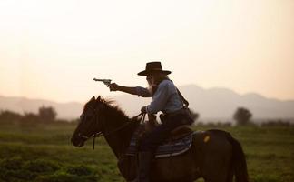 siluett cowboy på hästryggen mot en vacker solnedgång, cowboy och häst vid första ljuset, berg, flod och livsstil med naturligt ljus bakgrund foto