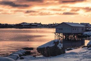 stuga med fiskeläge vid kusten vid solnedgången på Lofotenöarna foto