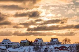 solsken i moln över skandinavisk fiskeläge med snö foto