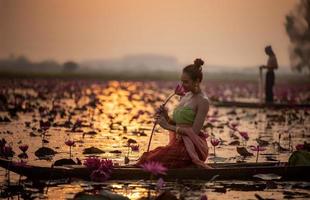 unga asiatiska kvinnor i traditionell klädsel i båten och rosa lotusblommor i dammen. vackra flickor i traditionell kostym. thailändsk flicka i retro thaiklänning, thailändsk flicka i traditionell dräkt foto