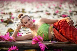 unga asiatiska kvinnor i traditionell klädsel i båten och rosa lotusblommor i dammen. vackra flickor i traditionell kostym. thailändsk flicka i retro thaiklänning, thailändsk flicka i traditionell dräkt foto