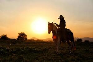 siluett cowboy på hästryggen mot en vacker solnedgång, cowboy och häst vid första ljuset, berg, flod och livsstil med naturligt ljus bakgrund foto