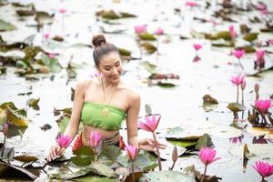 unga asiatiska kvinnor i traditionell klädsel i båten och rosa lotusblommor i dammen. vackra flickor i traditionell kostym. thailändsk flicka i retro thaiklänning, thailändsk flicka i traditionell dräkt foto