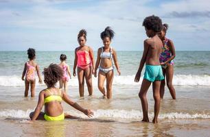 barn som leker springer på sand på stranden, en grupp barn håller händerna i rad på stranden på sommaren, bakifrån mot havet och blå himmel foto