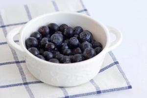 vit skål med blåbär på en ljus bakgrund. lätt matfotografering ovanifrån