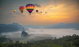 färgglada luftballonger flyger över berg och hav av dimma i soluppgången. berg med luftballonger på morgonen. foto