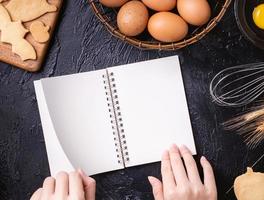 kvinnan läser kokboksrecept för att göra halloweenkakor med bakningsingredienser, designkoncept för matlagningskurs, ovanifrån, platt lay, overhead. foto