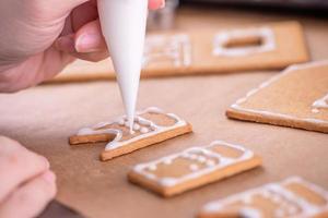 kvinnan dekorerar pepparkakshus med vit glasyrtoppning på träbordsbakgrund, bakpapper i köket, närbild, makro. foto