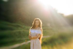 porträtt av en ung vacker flicka i en solklänning. sommarfotosession i parken vid solnedgången. en flicka sitter under ett träd i skuggan. foto