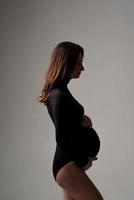 ung vacker gravid kvinna i svart bodysuit och hatt. foto