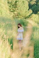 porträtt av en ung vacker flicka i en solklänning. sommarfotosession i parken vid solnedgången. en flicka sitter under ett träd i skuggan. foto