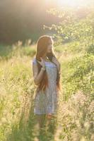 porträtt av en ung vacker flicka i en solklänning. sommarfotosession i parken vid solnedgången. en flicka sitter under ett träd i skuggan. foto