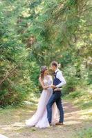 ett attraktivt nygift par, en lycklig och glädjefull stund. en man och en kvinna rakar sig och kysser sig i semesterkläder. bröllopscermonia i bohemisk stil i skogen i frisk luft. foto