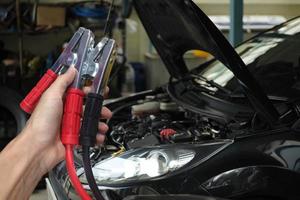 hand som håller bilbatteriladdare över suddig bil i garagebakgrund foto